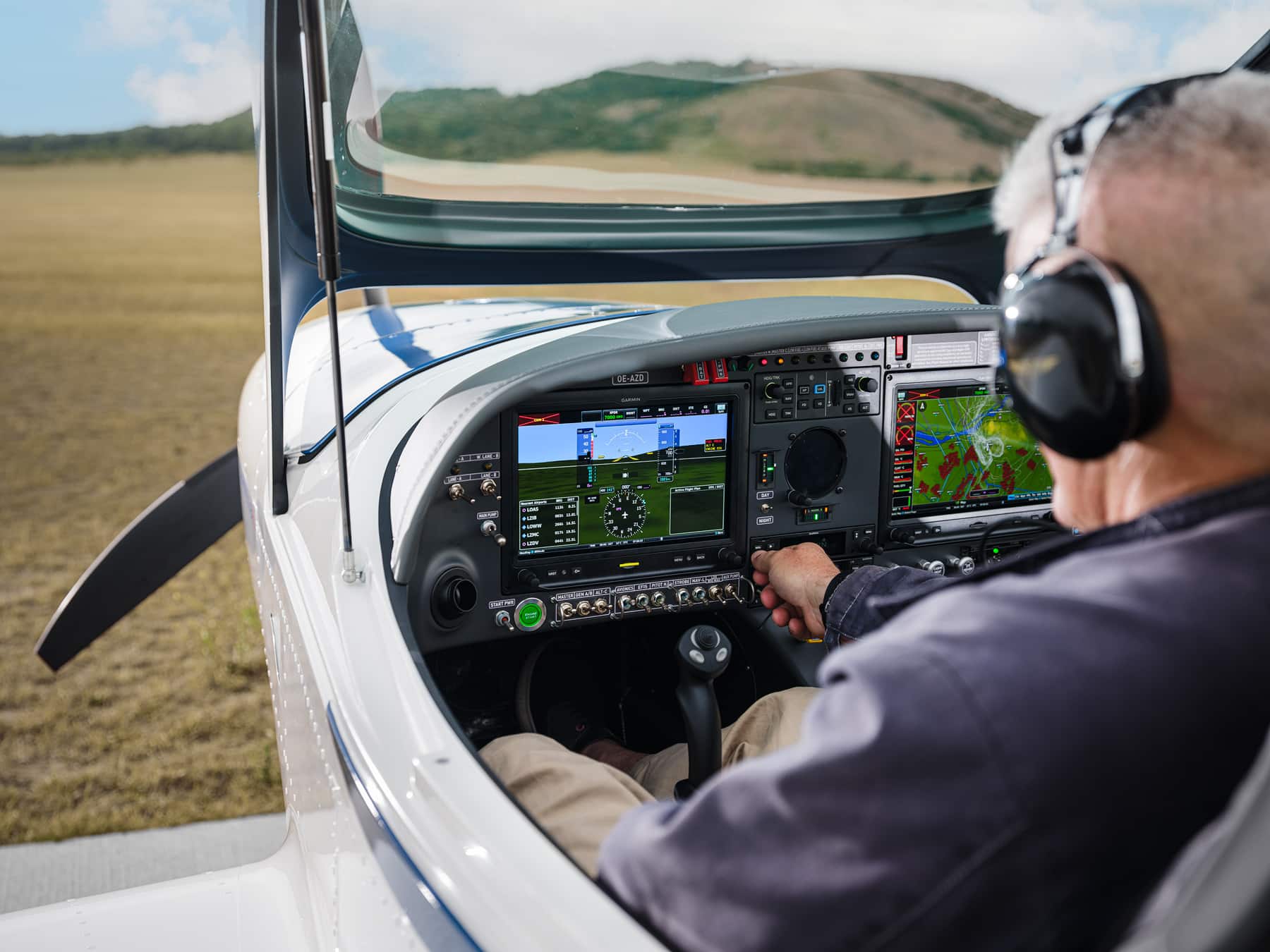 Pilot im Cockpit eines modernen Kleinflugzeugs am Spitzerberg, Blick auf digitales Cockpit mit Navigationsanzeigen, während das Flugzeug am Boden vor hügeliger Landschaft steht