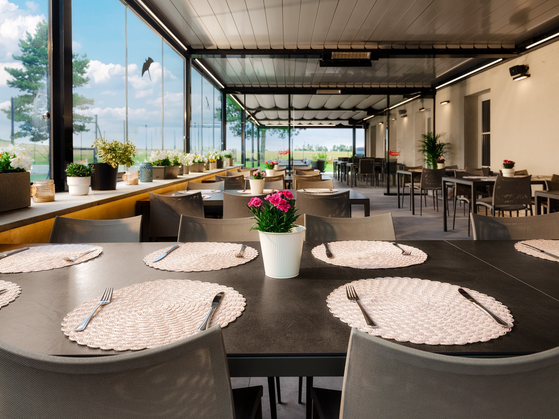 Überdachte Restaurantterrasse mit modern gedeckten Tischen, Stühlen und Blumen, hellem Innenhofblick durch große Glasflächen am Spitzerberg